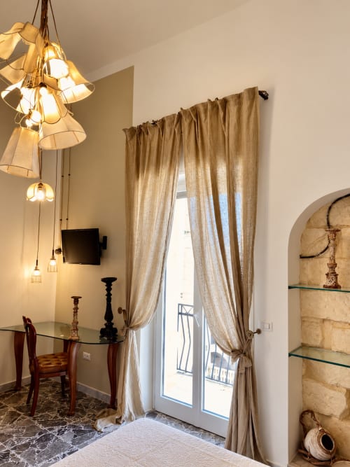 Elegante camera superior all'HABITARE Lecce con sospensioni di design, scrivania in legno, tende beige e accesso al balcone