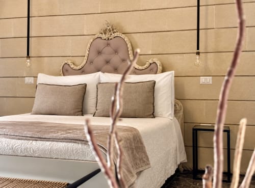 Camera elegante presso HABITARE Lecce con testata ornamentale color crema, cuscini trapuntati beige, biancheria bianca e luci pendenti