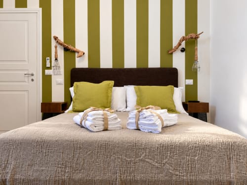 Olivum double room at HABITARE Lecce with olive-striped walls, green pillows, wooden bedside lamps, and fresh towels on beige