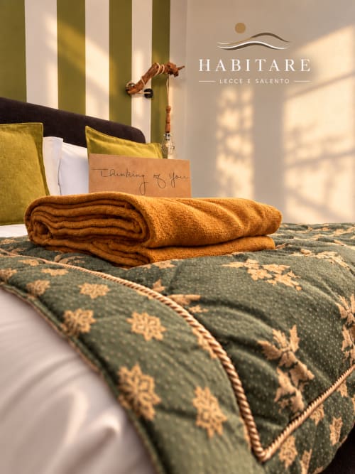 Cozy HABITARE Lecce bedroom with folded golden blanket, striped green walls, and welcome note on bed