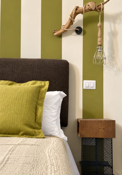 Olivum room at HABITARE Lecce featuring green striped walls, dark upholstered bed with yellow pillow, and wooden nightstand
