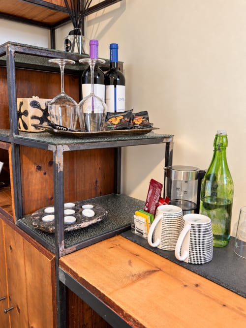 Hospitality welcome bar setup at HABITARE Lecce with wine glasses, bottles, snacks, and amenities on rustic wooden shelf