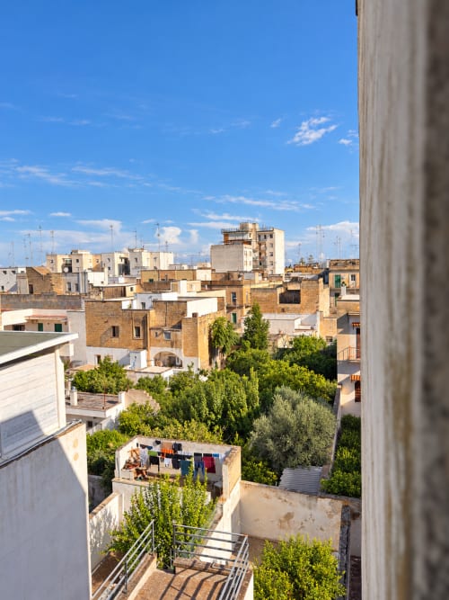 View from Olivum room at HABITARE Lecce showing historic Lecce rooftops, terracotta buildings, and lush gardens under blue