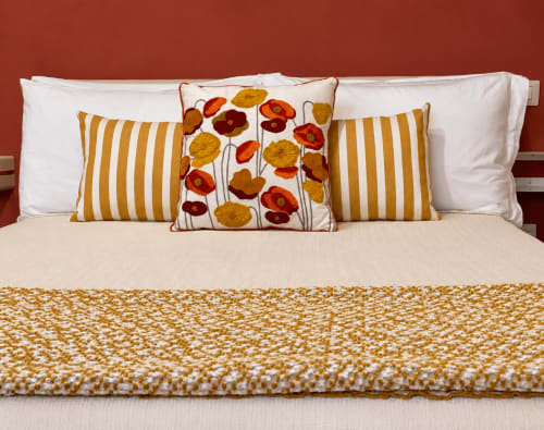 Letto accogliente presso HABITARE Lecce con biancheria bianca, cuscini a righe dorate e plaid floreale con papaveri rossi e gialli