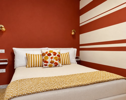 Cozy hotel bedroom at HABITARE Lecce with red and white striped walls, gold accents, and colorful floral pillows