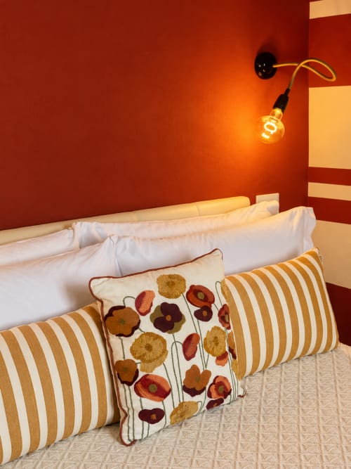 Cozy double bed with striped and floral pillows in Rubrum room at HABITARE Lecce, red accent wall with vintage pendant light