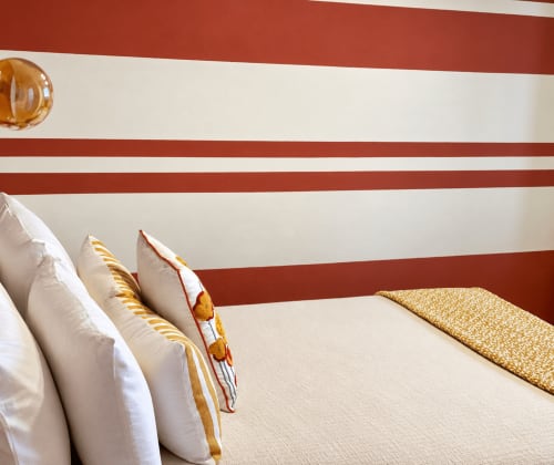 Cozy double bedroom at HABITARE Lecce with red and white striped headboard, decorative pillows, and mustard accents