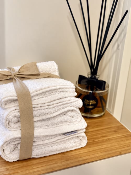 Rolled white towels tied with beige ribbon and amber diffuser on wooden shelf at HABITARE Lecce boutique hotel