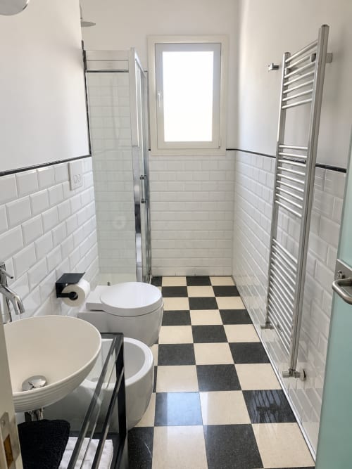 Modern bathroom at HABITARE Lecce with checkered tile floor, white subway tiles, pedestal sink, toilet, and heated towel rack