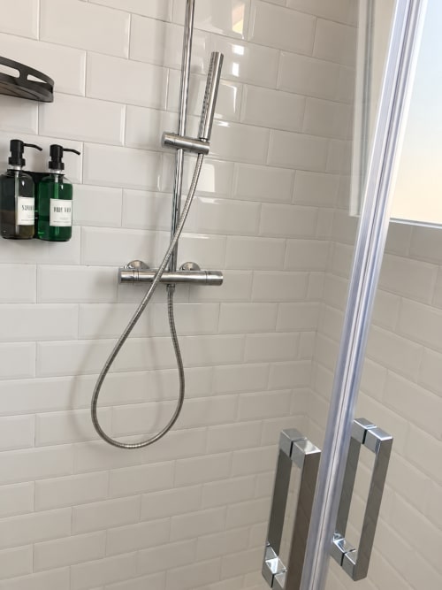 Modern shower in HABITARE Lecce hotel with chrome fixtures, white subway tiles, and toiletries on shelf