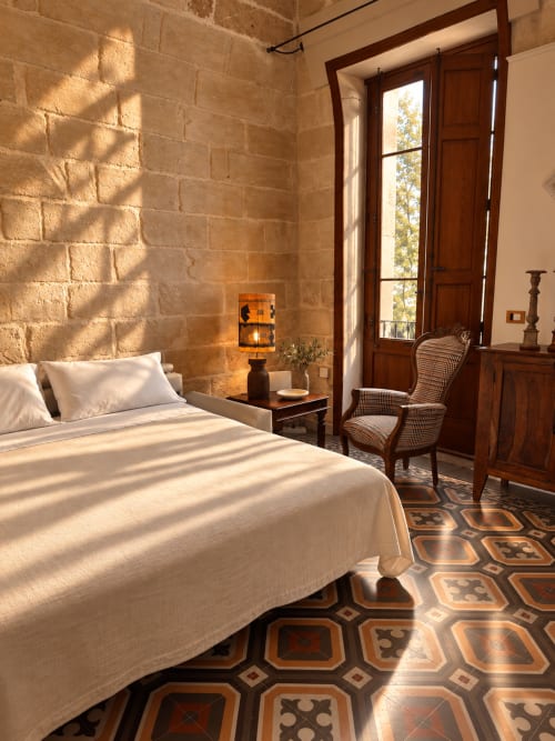 Sunny bedroom at HABITARE Lecce with terracotta brick walls, white bedding, geometric tile floor, and French doors opening to