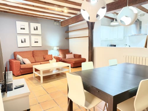 Sala de estar y comedor diáfano Stay Gest Valencia con sofá naranja, vigas de madera y mobiliario moderno