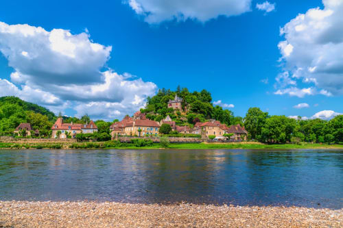Hôtel les Vieilles Pierres, village riverside aux bâtiments en pierre historiques, collines vertes ondulantes et ciel bleu dégagé