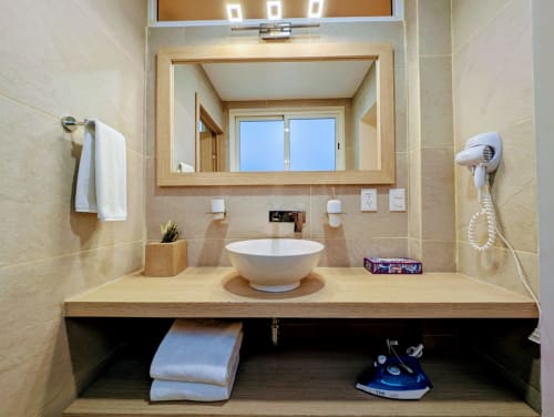 Baño moderno con lavamanos redondo blanco, espejo con marco de madera y azulejos color crema en el hotel Casa Donceles de Ciudad de México