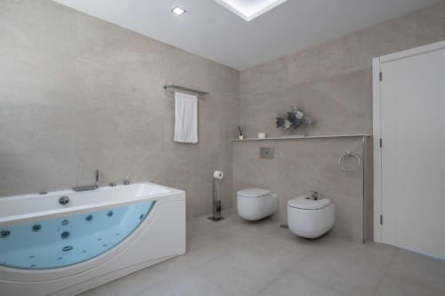 Modern bathroom at Manage Home Tenerife with jacuzzi tub, white fixtures, and beige tile walls in Costa Adeje apartment