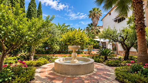 Serene garden courtyard at Casa Rural Garden Suites in Xàtiva with stone fountain, palm trees, and blooming flowers