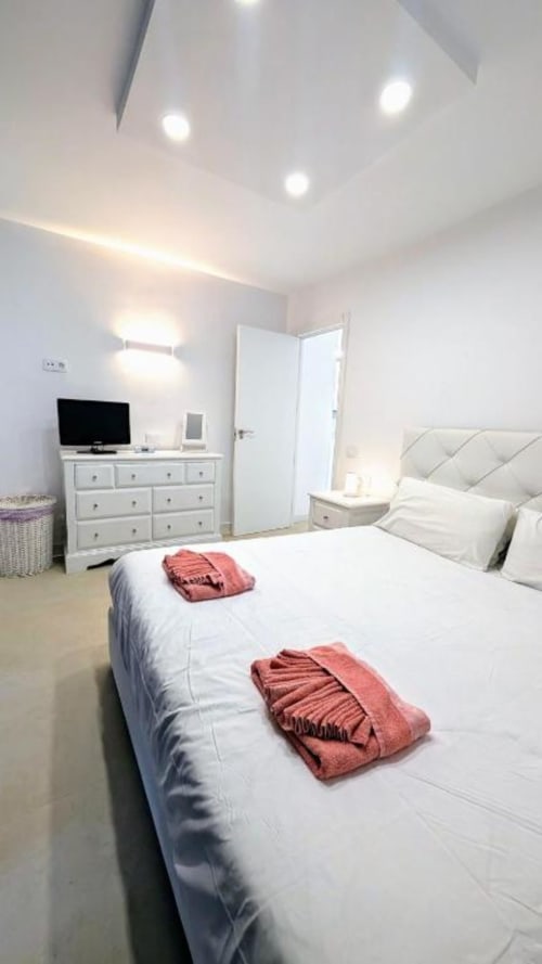 Modern bedroom with white furnishings, red towels on bed, TV, and recessed ceiling lights at Manage Home Tenerife apartment