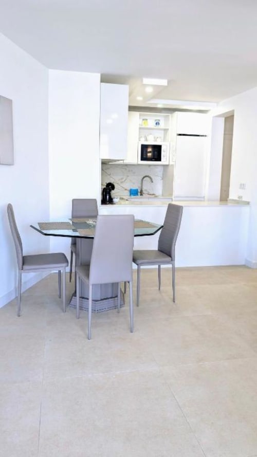 Modern apartment kitchen and dining area with glass table and gray chairs in Playa de las Américas, Tenerife