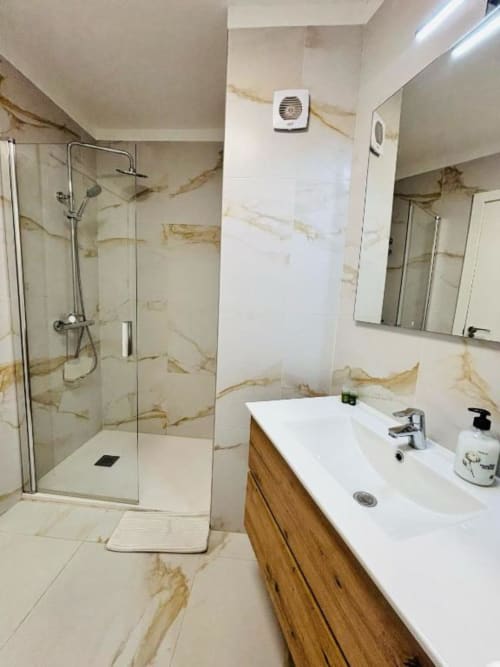 Modern bathroom in Playa de las Américas apartment with marble-patterned tiles, walk-in shower, wooden vanity, and large