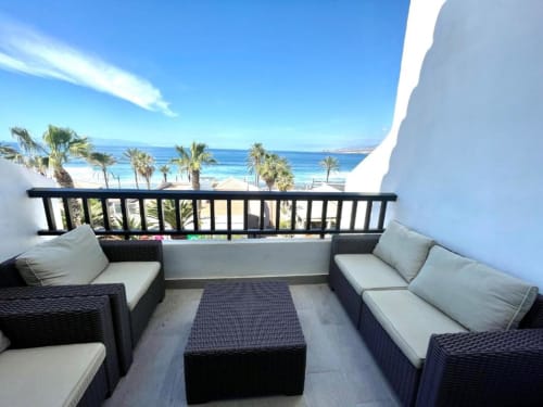 Beachfront apartment balcony with sea view in Playa de las Américas, featuring modern black rattan furniture and palm trees