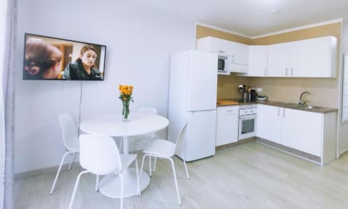 Modern apartment kitchen and dining area with white cabinetry, round table, and wall-mounted TV at Manage Home Tenerife in