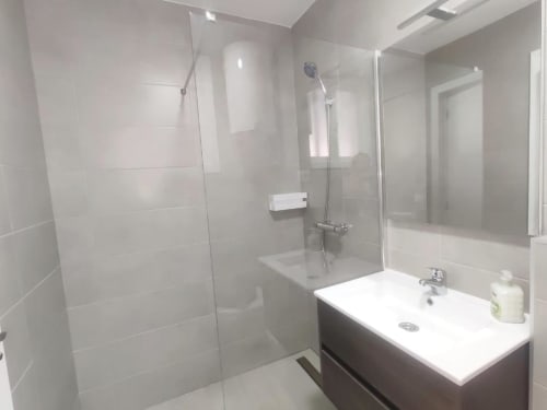 Modern bathroom in Manage Home Tenerife apartment with glass shower enclosure, white sink vanity, and light tiled walls