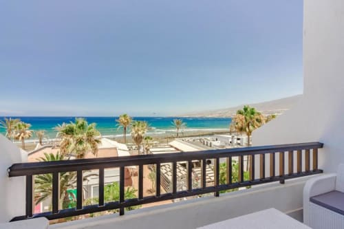 Balcony view of Playa de las Américas beach with turquoise ocean, palm trees, and white buildings in Tenerife