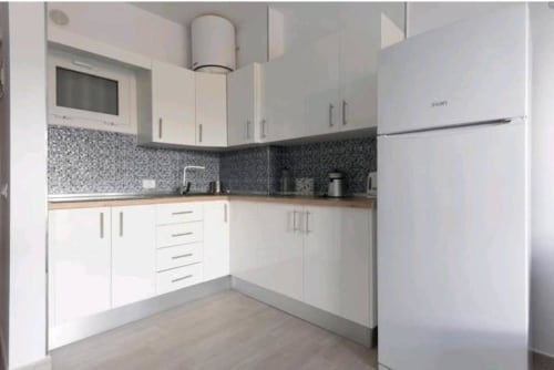 Modern white kitchen with mosaic backsplash, wooden counters, and stainless steel appliances at Manage Home Tenerife