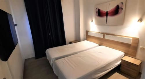 Modern bedroom at Manage Home Tenerife apartment in Los Cristianos with twin beds, wood headboard, and red dragonfly wall art