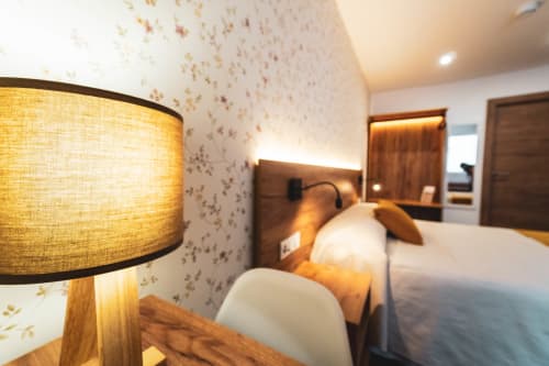 Moderna habitación doble en la Hospedería Ángel con iluminación cálida, papel tapiz decorativo y muebles de madera en Huelma, Jaén