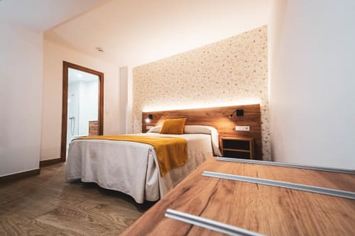 Moderno dormitorio doble en Hospedería Angel de Huelma con cabecero de madera, almohada dorada y detalle en azulejo terracota