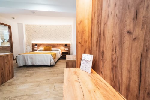 Moderna habitación doble en Hospedería Angel de Huelma con muebles de madera, cama con detalles amarillos y zona de escritorio de madera