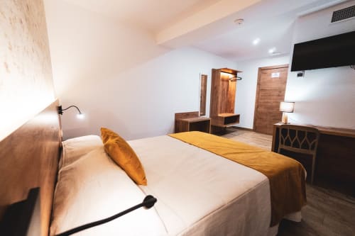 Moderna habitación doble de la Hospedería Angel en Huelma con cama queen, muebles de madera y TV de pantalla plana