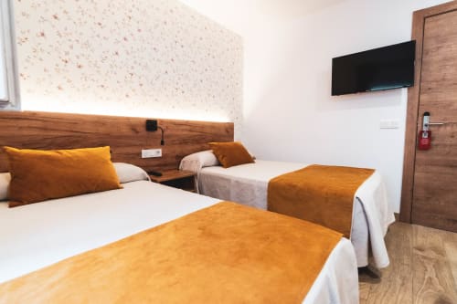 Habitación moderna en Hospedería Angel con dos camas individuales, detalles en naranja, televisor de pantalla plana y cabecero de madera en Huelma,