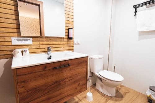 Cuarto de baño moderno de la Hospedería Ángel en Huelma con mueble de madera, lavabo blanco, inodoro y espejo