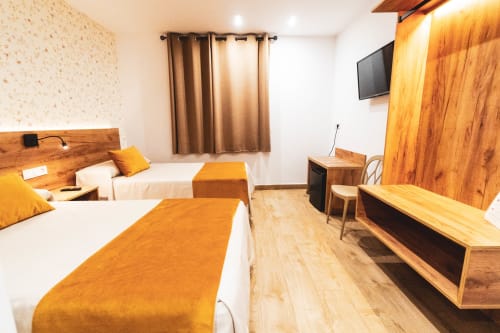Habitación doble en Hospedería Angel de Huelma con dos camas, muebles de madera, detalles naranjas y TV pantalla plana.