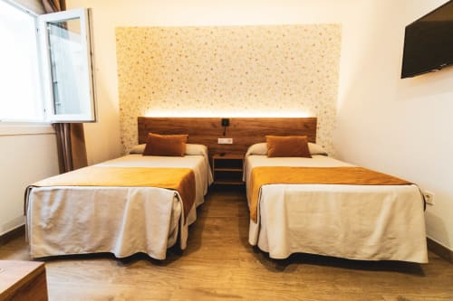 Habitación doble en Hospedería Angel hotel en Huelma con dos camas, cabecero de madera y pared de acento en terracota cálido.