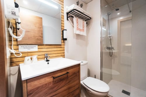 Baño moderno del hotel Hospedería Angel en Huelma con tocador de madera, lavabo blanco, ducha de cristal y toallero radiante