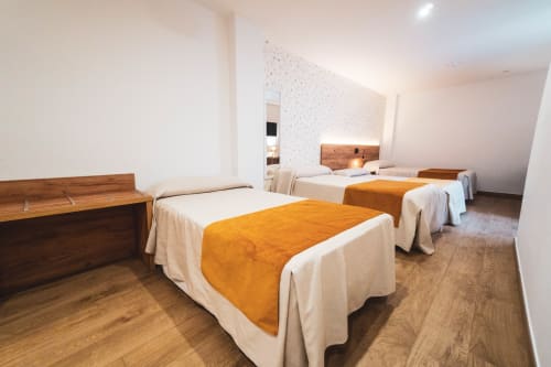 Amplia habitación cuádruple en Hospedería Angel con cuatro camas, muebles de madera, mantas naranjas y suelo de madera
