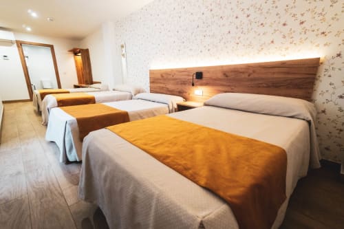Habitación Superior con cuatro camas en Hospedería Angel, Huelma, con cabecero de madera y caminos de cama naranjas