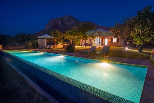 Villa de lujo iluminada Can Jaumí en Artá con piscina luminosa, terraza, tumbonas y vistas a la montaña al atardecer