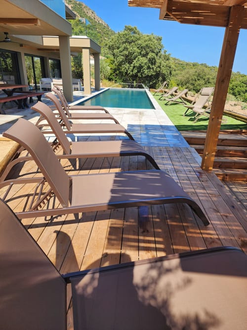 Chaises longues de luxe sur terrasse en bois avec vue privée sur la piscine et paysage verdoyant aux Villas d'A Storia, Pinarellu