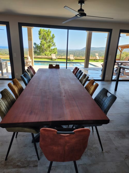 Salle à manger contemporaine avec longue table en bois et chaises colorées face à piscine privée et vue sur mer à Villa Aria Terra