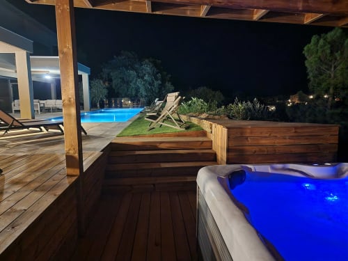 Terrasse de villa luxe la nuit avec jacuzzi illuminé, piscine chauffée, terrasse en bois et vue mer à Pinarellu, Corse