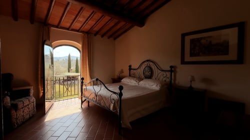 Camera da letto al Borgo di Erboli a Cavriglia con letto in ferro battuto, vista terrazza tra cipressi, travi in legno e stile tradizionale