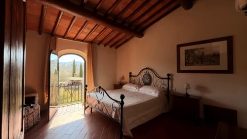 Camera da letto dell'appartamento Cosimo a Borgo di Erboli, Cavriglia, con letto in ferro battuto, muri in terracotta, travi a vista e stile toscano