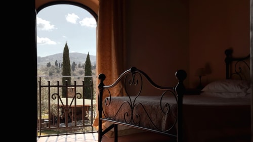 Camera da letto nel Borgo di Erboli a Cavriglia con letto in ferro battuto, muri in terracotta e vista sul paesaggio toscano attraverso l'arco
