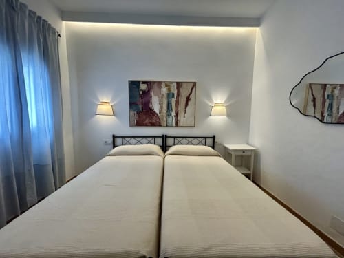 Dormitorio de apartamento moderno en Sevilla con dos camas, iluminación ambiental, obras de arte y mobiliario contemporáneo
