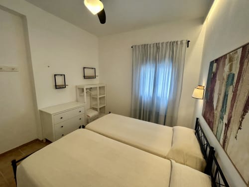 Dormitorio luminoso con dos camas individuales, muebles blancos y ventanas con cortinas translúcidas en apartamento Judería3, Sevilla