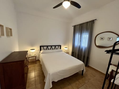 Dormitorio luminoso en apartamento CozyHomeSevilla Sevilla con cama blanca, cabecero negro, lámparas de mesita, ventilador de techo y gris